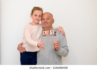 Holiday. Happy Family. Portrait Of Handsome Old Man Grandpa Smiling Having Fun With His Cute Funny Granddaughter. Girl And Dad Wearing Sweater Holding Word Love. Grandfather Hugging His Grandchild.