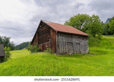 Holiday house on steep slope and rocky mountain in background. Cabin on green pasture and edge of forest with single tree in Rhein valley under Alpstein. wooden hut or barn on interesting cloudy day - Powered by Shutterstock