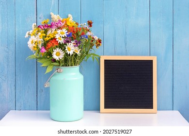 Holiday Mock Up. Empty Blank Black Letter Board And Bouquet Of Bright Flowers In Tin Can Vase On Table Against Blue Wooden Wall. Front View, Mockup.