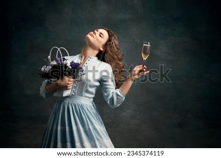 Holiday mood. Dreaming aristocratic relaxing woman wearing blue historical dress and dancing with glass of shampagne and bunch of flowers. Concept of healthy lifestyle, diet, style, fashion.