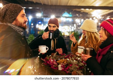 Holiday New Year's Atmosphere. Happy Smiling Friends With Cups Of Hot Drinks, Mulled Wine Talking, Spending Time Together At Winter Fair At Evening. Enjoying, Dressing Warmly, Looking At Each Other