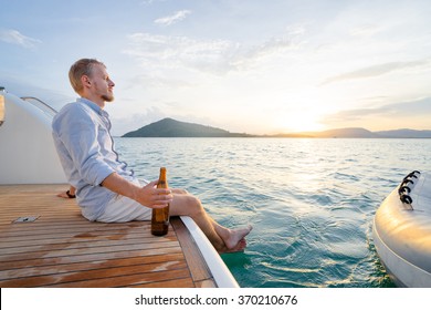 Holiday on the sea. Relaxed young man with beer bottle sitting on the yacht deck.