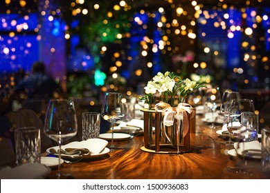 Holiday Party Blurred Background Made From Decorated Table With Bouquet Of Flowers And Colorful Lights Bokeh. Selective Focus. Christmas Dinner, New Year, Birthday, Wedding Party Table Setting.