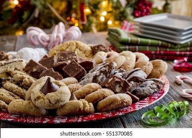 Holiday Party Table With Homemade Cookie Tray, White Plates And Holiday Napkins In Front Of Christmas Tree