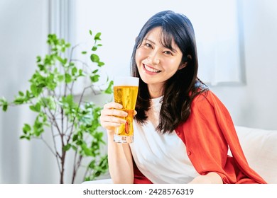 As a holiday pleasure, a Japanese woman looking at a camera in her 20s and 30s with a full smile of drinking glass beer from noon at home