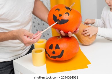 Holiday Preparation And Handmade Party Decor. Halloween Family Indoor Activity, Pumpkin Painting Process. Spooky Smile Of Jack-o-lantern. Drawing Scary Face