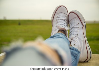 Holiday  relax female legs in jeans with ankle height sneakers. Female legs white wearing trainers. Ripped jeans legs - Powered by Shutterstock