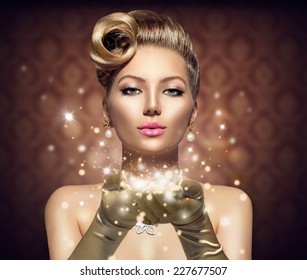 Holiday Retro Woman Blowing Magic Dust In Her Hand. Beauty Fashion Christmas Vintage Style Lady With Beautiful Luxury Hairstyle, Makeup, Accessories. Golden Silk Gloves And Dress 