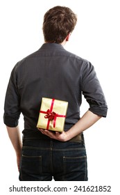 Holiday And Special Occasion. Man Giving Golden Gift Box With Red Ribbon Isolated On White. Guy Hiding Present Behind His Back. Surprise. Studio Shot.