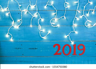 Holiday String Of Lights And Year 2019  In Bold Red Hanging On Rustic Teal Blue Wood Sign; Christmas Background With Copy Space