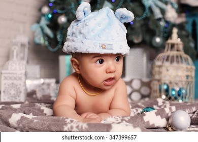 holiday tender photo of cute little baby in funny hat lying beside Christmas tree with a lot of presents  Foto Stok