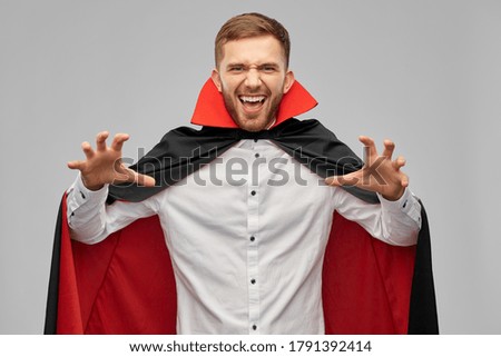 holiday, theme party and people concept - man in halloween costume of vampire and dracula cape scaring over grey background