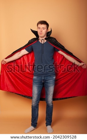 holiday, theme party and people concept - happy smiling man in a vampire costume for Halloween and Dracula's cloak with a spider in his hands for the holiday