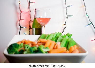 Holiday vegtable tray with alcoholic beverages and festive holiday lighting on a white background. Vegtables inclue carrots, broccoli, and celery sticks.