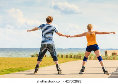 Holidays, active people and friendship concept. Young fit couple on roller skates riding outdoors on sea coast, woman and man rollerblading together on the promenade - Powered by Shutterstock