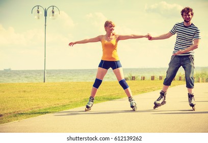 Holidays, active people and friendship concept. Young fit couple on roller skates riding outdoors on sea shore, woman and man rollerblading together on the promenade - Powered by Shutterstock
