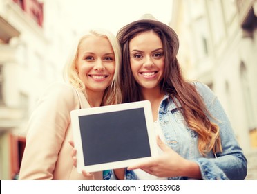 holidays, advertisement, technology and tourism concept - two beautiful girls toursits with blank screen tablet pc in the city