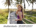 Holidays in Aracaju, Brazil. Portrait of attractive Brazilian female model with purple tank top walking on path to the sea in Aracaju at sunset, Sergipe, Brazil.