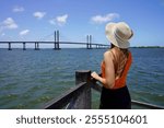 Holidays in Aracaju, Brazil. Rear view of young woman on pier in Aracaju with Ponte Joao Alves bridge on the background, Brazil.