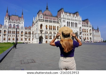 Holidays in Budapest. Back view of beautiful stylish girl enjoying view of Hungarian Parliament Building in Budapest, Hungary. Tourism in Europe.