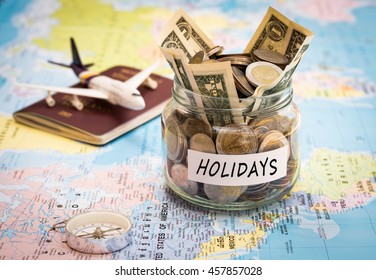 Holidays budget concept. Holidays money savings in a glass jar with compass, passport and aircraft toy on world map