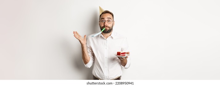 Holidays And Celebration. Cheerful Man Enjoying Birthday, Blowing Party Whistle And Holding Bday Cake, White Background