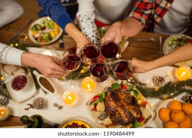 Holidays And Celebration Concept - Close Up Of Friends Having Christmas Dinner At Home, Drinking Red Wine And Clinking Glasses