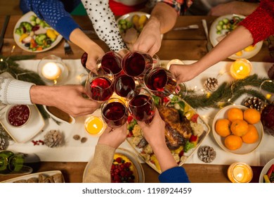 Holidays And Celebration Concept - Close Up Of Friends Having Christmas Dinner At Home, Drinking Red Wine And Clinking Glasses