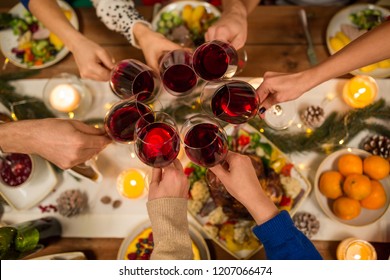 Holidays And Celebration Concept - Close Up Of Friends Having Christmas Dinner At Home, Drinking Red Wine And Clinking Glasses