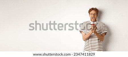 Holidays and celebration concept. Funny redhead guy blowing candle on birthday cake, smiling and making wish, white background.