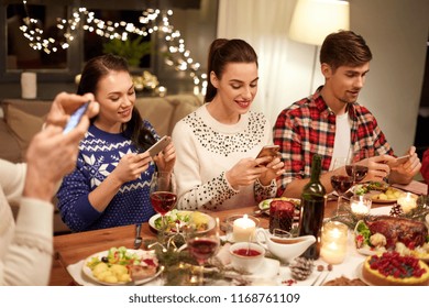 holidays and celebration concept - happy friends with smartphones having christmas dinner at home - Powered by Shutterstock