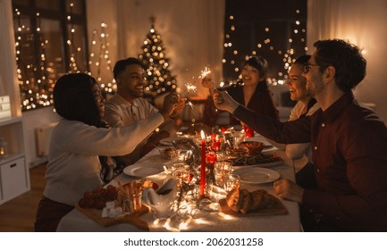 holidays and celebration concept - multiethnic group of happy friends with sparklers having christmas dinner at home - Powered by Shutterstock