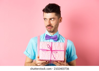 Holidays And Celebration Concept. Shocked Guy Staring Aside With Cringe Face, Holding Small Gift Box, Standing Over Pink Background