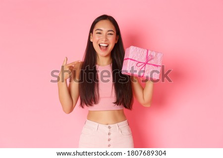 Holidays, celebration and lifestyle concept. Beautiful happy asian girl pointing at herself, its her birthday, receive gift wrapped in pink paper, smiling broadly over studio background