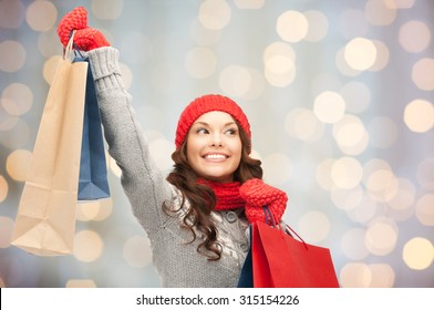 holidays, christmas, sale and people concept - happy young asian woman in winter clothes with shopping bags over lights background