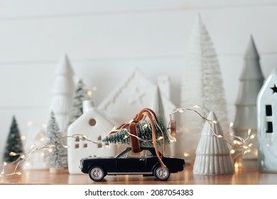 Holidays coming! Festive Christmas scene, miniature holiday village. Car with christmas tree, little houses and snowy trees on white background. Merry Christmas and Happy New Year !