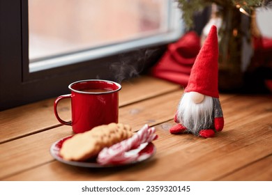 holidays, decoration and celebration concept - close up of christmas gnome, cup of coffee in red mug, ginger cookies and candy canes on window sill at home - Powered by Shutterstock