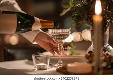 holidays, dinner party and celebration concept - close up of hand pouring champagne from bottle to glass on table at home or restaurant