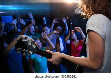 Holidays, Music, Nightlife And People Concept - Close Up Of Singer Playing Electric Guitar And Singing On Stage Over Happy Fans Crowd Waving Hands At Concert In Night Club