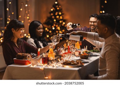 holidays, party and celebration concept - multiethnic group of happy friends having christmas dinner at home and drinking wine - Powered by Shutterstock