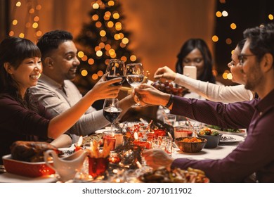 holidays, party and celebration concept - multiethnic group of happy friends having christmas dinner at home and drinking wine - Powered by Shutterstock