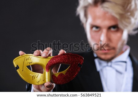 Holidays, people and celebration concept. Elegant young guy wearing suit white shirt bow tie and carnival venetian mask, on dark.