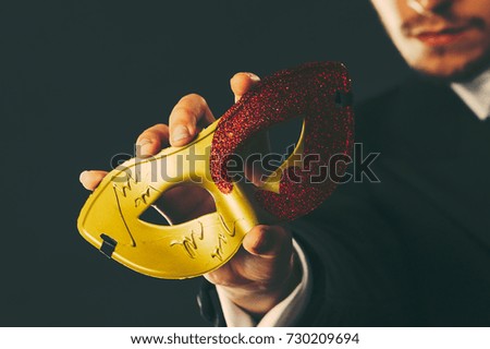 Holidays, people and celebration concept. Male hand holding red golden carnival mask closeup on dark