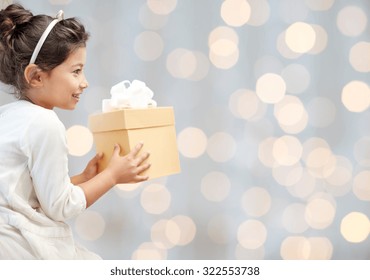 holidays, presents, christmas, childhood and people concept - smiling little girl with gift box over lights background