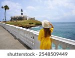 Holidays in Salvador de Bahia, Brazil. Rear view of girl with hat looking Forte Santo Antonio da Barra fort on promenade in the city of Salvador, Bahia, Brazil.