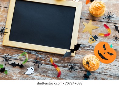 Holidays, School And Party Concept - Halloween Decorations And Treats With Blank Chalkboard On Wooden Boards Background