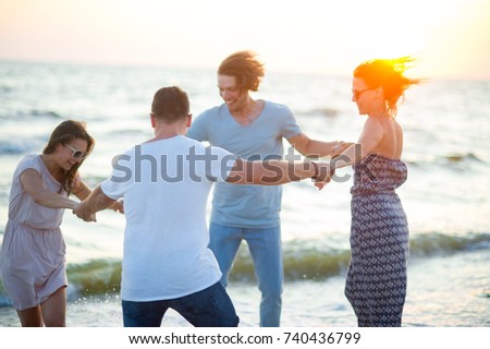 Holidays at the sea with friends. Group of cheerful young people dances having joined hands on the beach. Summer, waves, sea wind, sunset. Friends a lot of fun.
