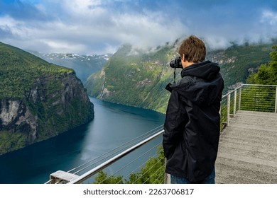 Holidays in southern Norway: the epic Geiranger Fjord - young man, teenager photographing the fjord from the viewpoint Ørnesvingen