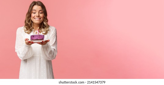 Holidays, spring and party concept. Portrait of dreamy, happy birthday girl feeling excitement and joy celebrating b-day, biting lip and smiling as making wish blowing candle on cake - Powered by Shutterstock