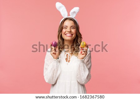 Holidays, spring and party concept. Portrait of lovely, cheerful blond girl in rabbit ears, holding colored eggs, celebrating Easter with family, enjoying spend traditional day with close people